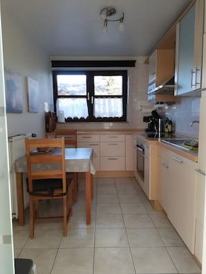 A kitchen with a dining table, chairs, cabinets, a window with curtains, and a view of the outside.