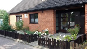 Un bâtiment en briques avec une porte noire, des fenêtres et un petit jardin agrémenté de plantes et de fleurs.