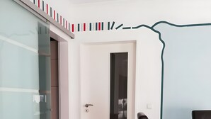Une pièce comprenant une table à manger en bois, une chaise noire, une porte avec un panneau de verre et un mur orné d’un simple dessin linéaire.