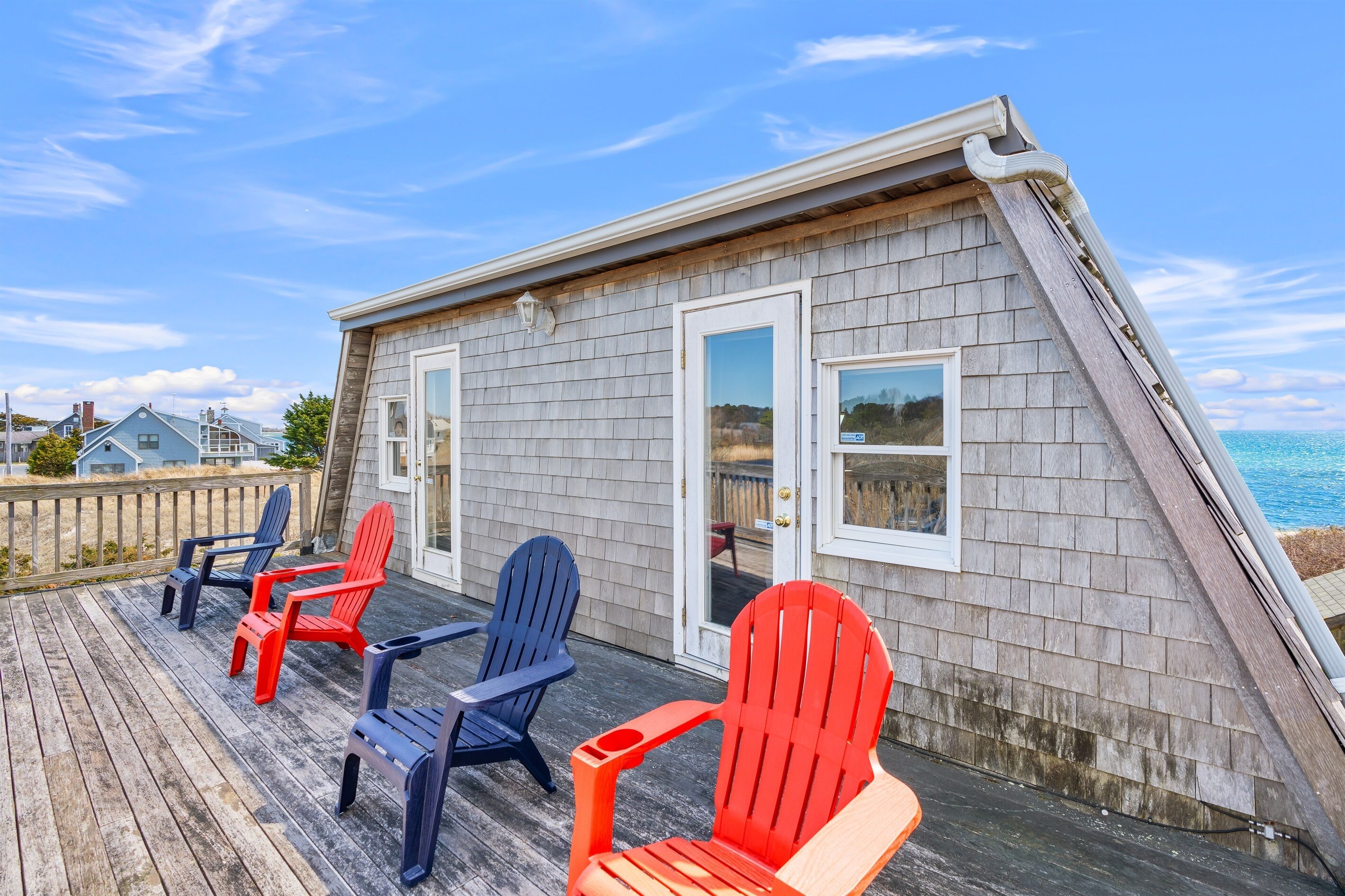 Een terras met Adirondack-stoelen en een huis met schuin dak, uitkijkend over de oceaan.
