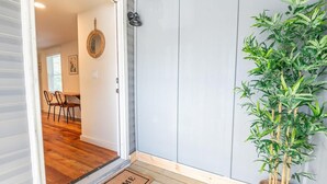 Ein Durchgang zu einem Zimmer mit Holzboden, einer Fußmatte, einem an der Wand befestigten Spiegel und einem Blumentopf.