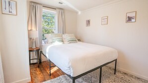 Ein Schlafzimmer mit Bett, Nachttisch, Lampe und einem Fenster mit Vorhängen.