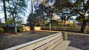 A wooden bench in a park with trees and a fence in the background.