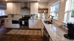 A kitchen with white cabinets, stainless steel appliances, a granite countertop, and a window providing natural light.