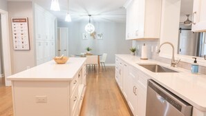 Una cocina moderna con armarios blancos, una isla central, un comedor con mesa y sillas, y un candelabro.