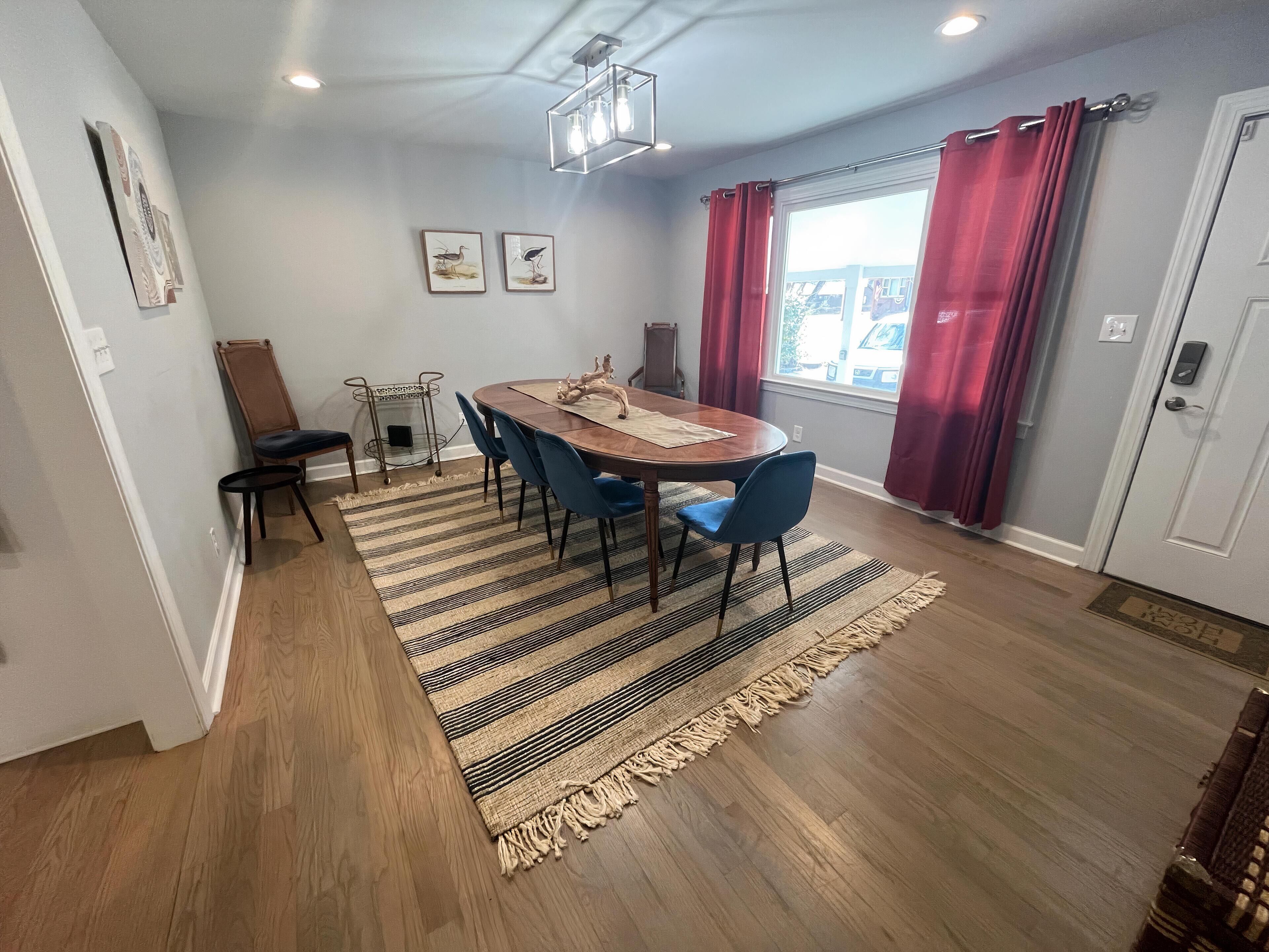 Un coin repas avec une table en bois, des chaises bleues, un tapis à rayures et un lustre.