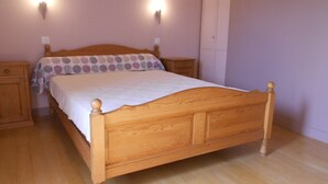 A neatly made wooden bed with a white bedspread and a polka dot pillow, flanked by two bedside tables with lamps, in a room with wooden flooring and light-colored walls. - Gîte Nelly en Cévennes (Molezon)