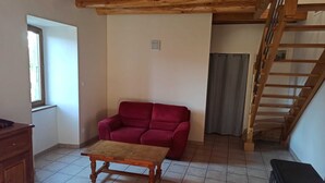 A room with a red sofa, a wooden table, a staircase, and a window. - Gîte Nelly en Cévennes (Molezon)