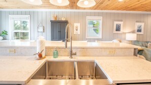 Une cuisine moderne dotée d’un grand îlot central, d’un évier en acier inoxydable et de luminaires suspendus.