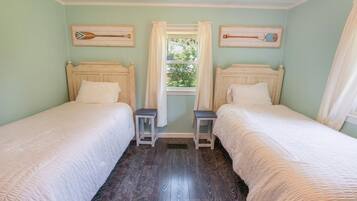 A room with two wooden beds, a window with curtains, and two wooden paddleboard paintings on the walls.