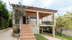 Una casa de dos pisos con un porche cubierto, una escalera que lleva a la entrada y un pequeño jardín.