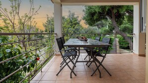 Un porche cubierto con una mesa y sillas, rodeado por una barandilla de metal, con vistas a un jardín con árboles y plantas.