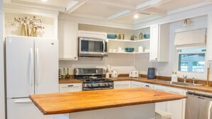 A modern kitchen with a central island, white cabinetry, stainless steel appliances, and a wooden countertop. - Paramount Paradise: Stylish + Screen Porch! (North Charleston)