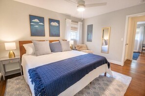Quarto com uma cama grande, mesa de cabeceira com abajur, cômoda e espelho na parede.