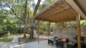 Eine Terrasse im Freien mit Holzboden, einer Pergola, Korbmöbeln und einem Grill.