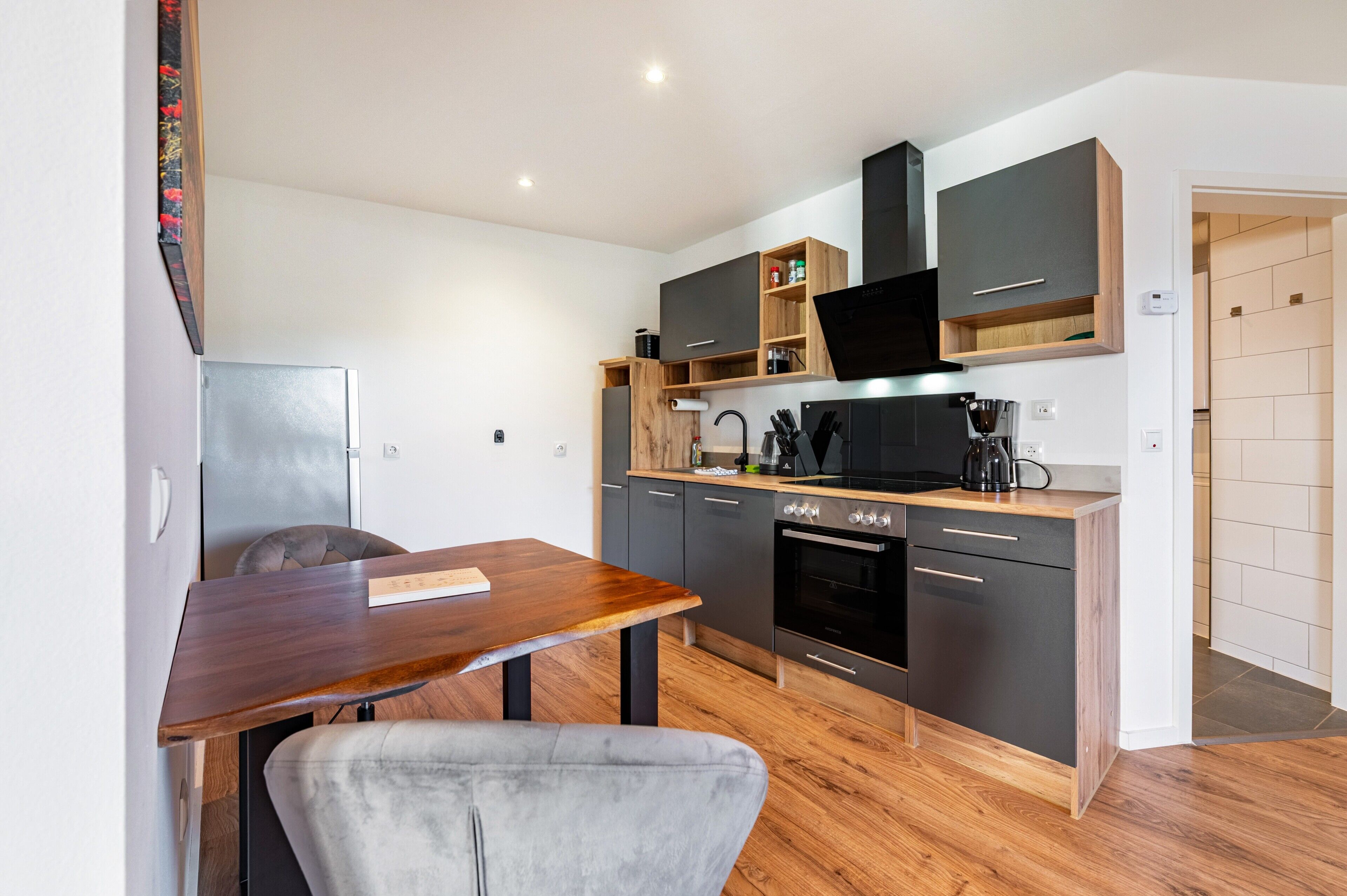 Een kleine keuken met een eethoek, met een houten tafel, een grijze stoel en moderne apparaten.