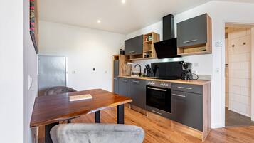 Een kleine keuken met een eethoek, met een houten tafel, een grijze stoel en moderne apparaten.