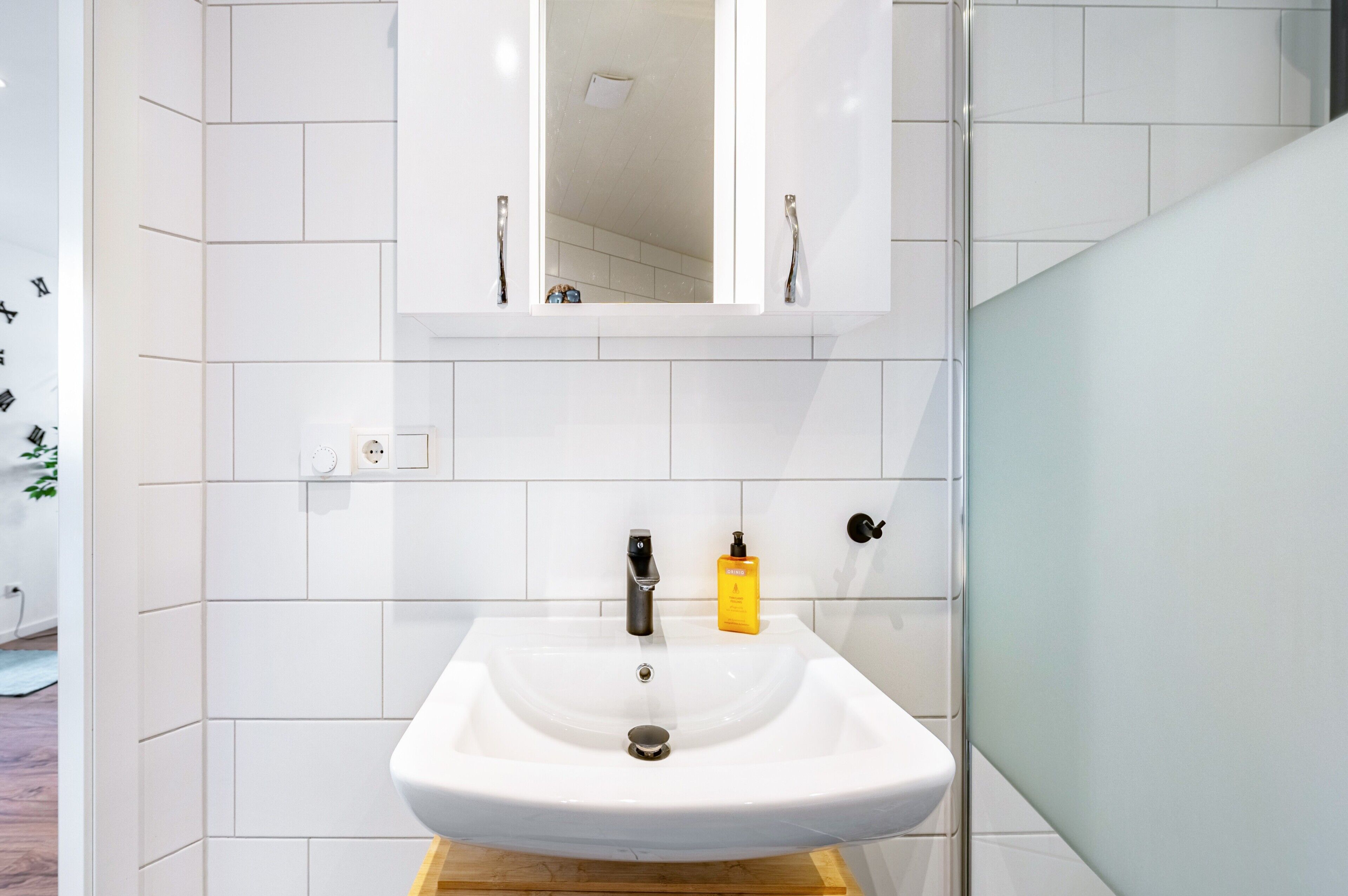 Een badkamer met een witte wasbak, een spiegel en een geel zeepdispenser.