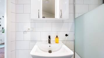Een badkamer met een witte wasbak, een spiegel en een geel zeepdispenser.