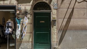 Eine grüne Tür mit Messingschild, ein Schaufenster voller Kleidung und eine Gebäudefassade mit Hausnummern.