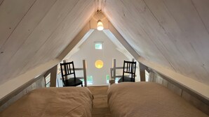 Une chambre mansardée avec de hauts plafonds, deux lits, des poutres en bois et une lucarne.