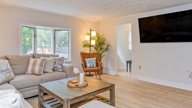 Una sala de estar con sofá, sillón, mesa de centro y televisor montado en la pared.