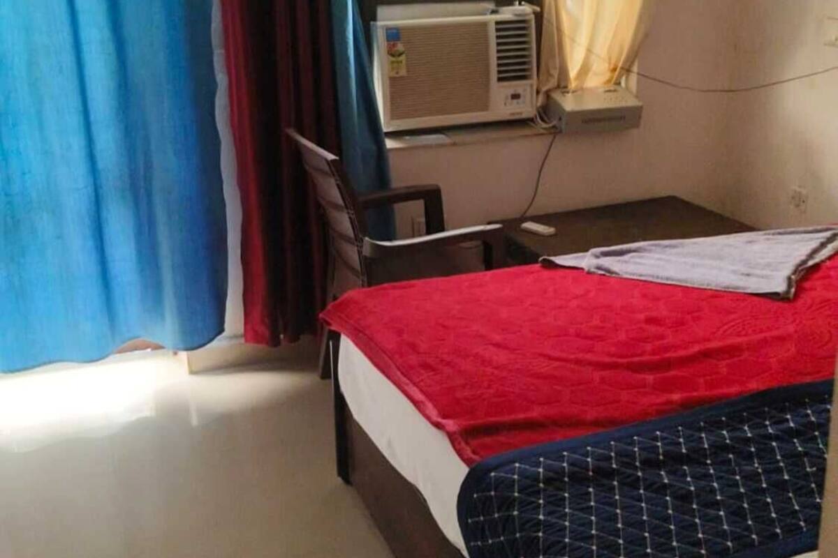 Una habitación con cama, una silla, ventana con cortinas y equipo de aire acondicionado.