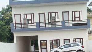 Un edificio de dos plantas con balcón en el piso superior, un coche estacionado frente a él y una entrada con portón.