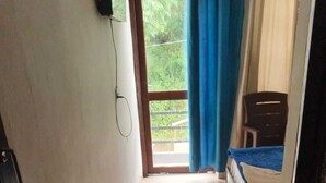 Un pasillo estrecho que conduce a un dormitorio con cama, una ventana con cortinas y una puerta.
