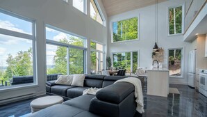 A modern kitchen with a central island, large windows, and a black leather sectional sofa.