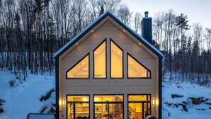 A modern house with large windows, a hot tub, and a bench in the snow.
