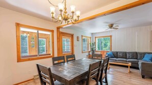 A dining area with a wooden table and chairs, a chandelier, and large windows with wooden frames. - Spa - Babyfoot | Le Panache (Entrelacs)