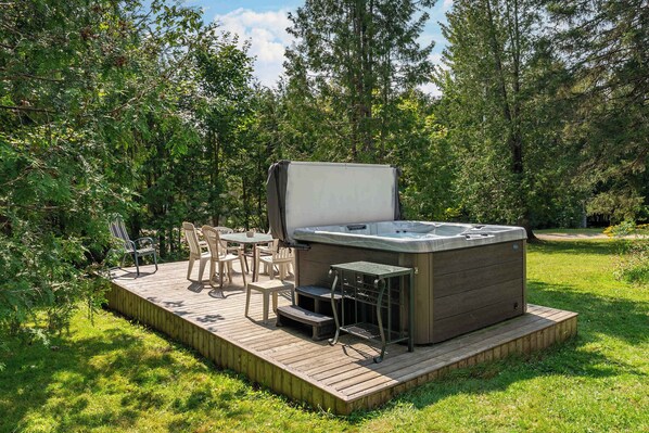 Un jacuzzi en una terraza de madera rodeado de follaje.