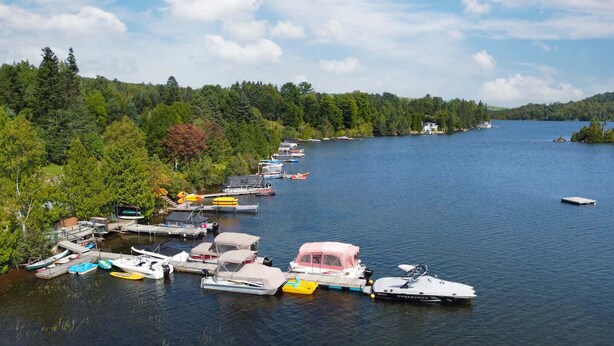 A marina with various boats docked along a calm lake surrounded by dense forest. - Spa - Babyfoot | Le Panache (Entrelacs)