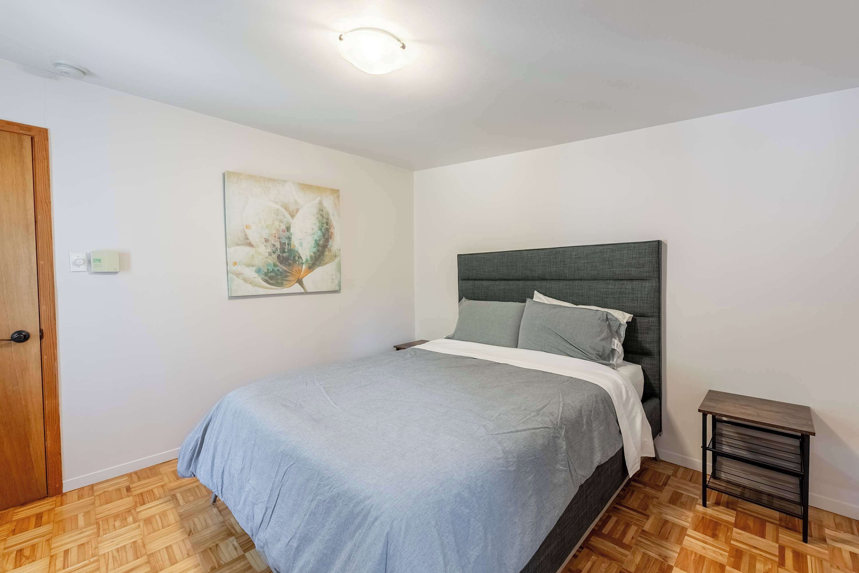 Une chambre à coucher comprenant un lit, une table de chevet, un radiateur fixé au mur et une porte.