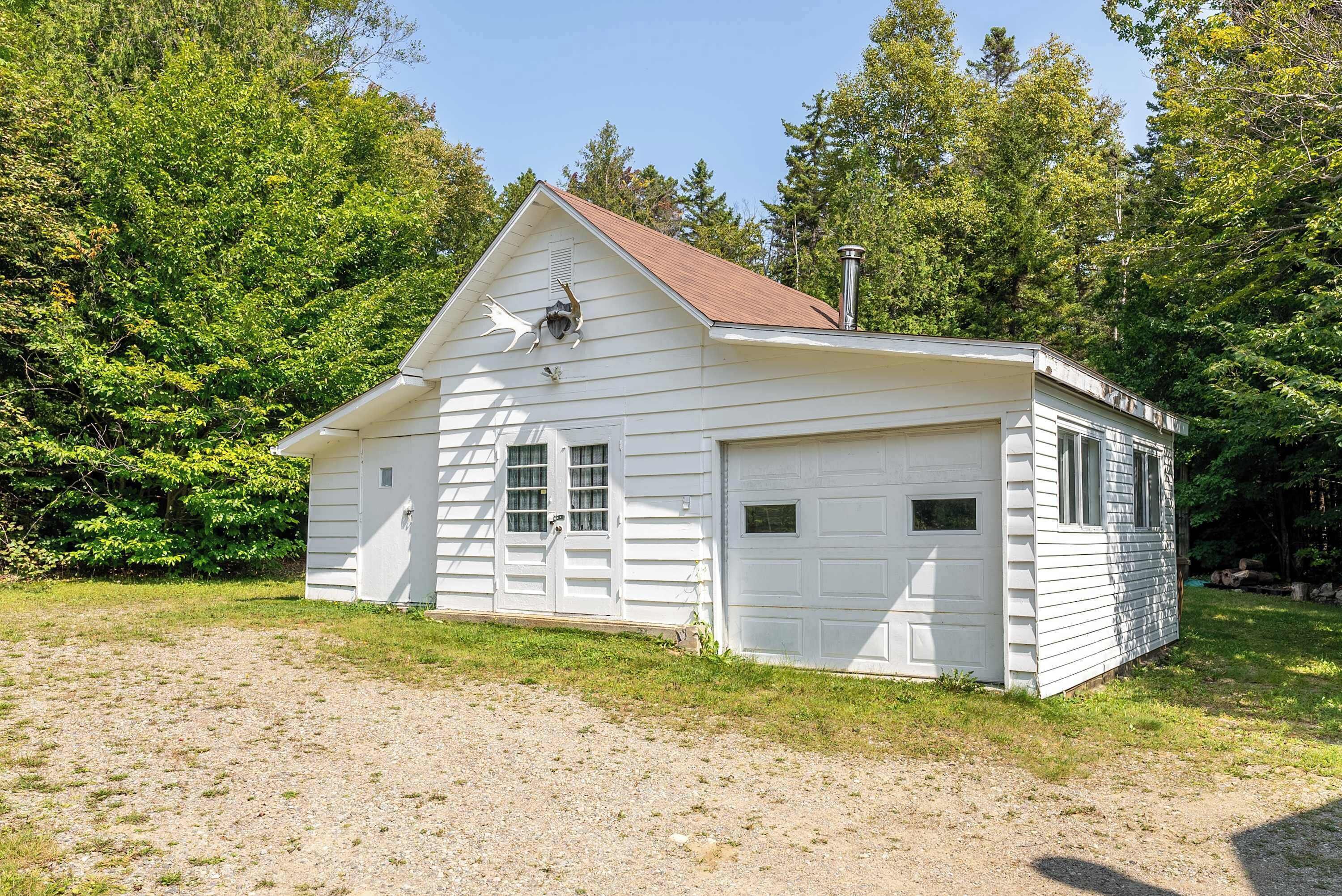 A white single-story building with a red roof, a garage, and a chimney.
