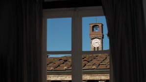 Blick durch ein Fenster auf ein Gebäude mit einem Glockenturm, bewölkten Himmel und einem Ziegeldach.