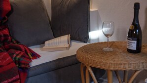 Ein gemütlicher Wohnbereich mit einer Couch, einem Korbtisch, einer Weinflasche und einem Glas.