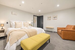 Una habitación de hotel moderna con cama, mesitas de noche, un banco, un sofá y obras de arte en las paredes.