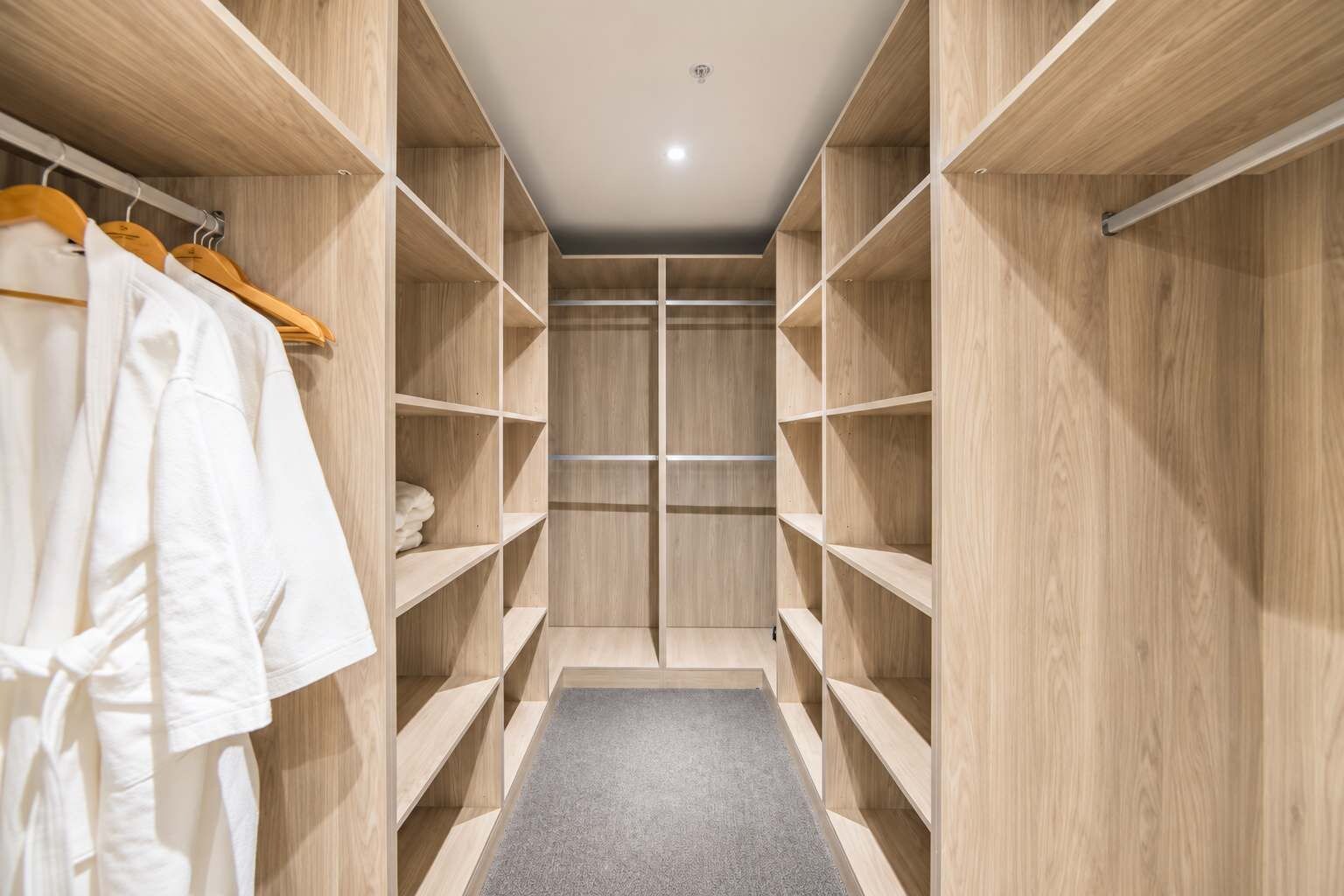 A walk-in closet with wooden shelving and a grey carpet.