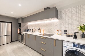Cozinha moderna com armários cinza, eletrodomésticos de aço inoxidável, máquina de lavar louça embutida e máquina de lavar roupa.