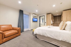 Habitación de hotel con cama, sofá de cuero, televisor y armario.