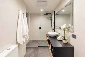 Un baño moderno con cabina de ducha de vidrio, un lavamanos blanco y un espejo encima.