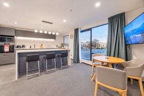 A modern kitchen with a bar area, a dining table with chairs, and a large window with curtains.