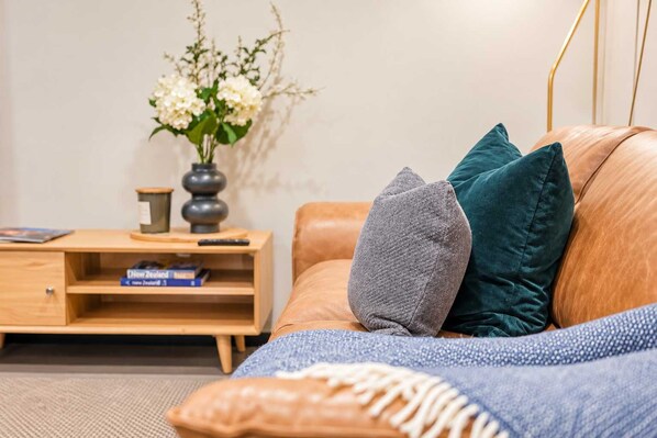 A modern living room with a leather sofa, a wooden side table with a vase of flowers, and a remote control.