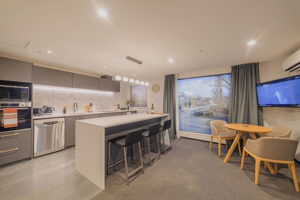 A modern kitchen with a central island, bar stools, and a dining area with a table and chairs.