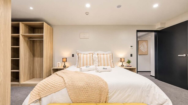 Un dormitorio con cama, lámparas de noche, un armario y una puerta que da a otra habitación.