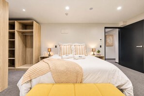 A bedroom with a bed, bedside lamps, a wardrobe, and a door leading to another room.