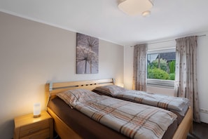 Una camera da letto con due letti, un comodino con una lampada, una finestra con tende e un'opera d'arte appesa al muro.
