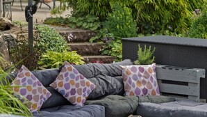 A garden setting with a grey outdoor sofa, patterned cushions, and a wicker basket. - Apartment 'Selbecke' with Pool and Garden (Kirchhundem)